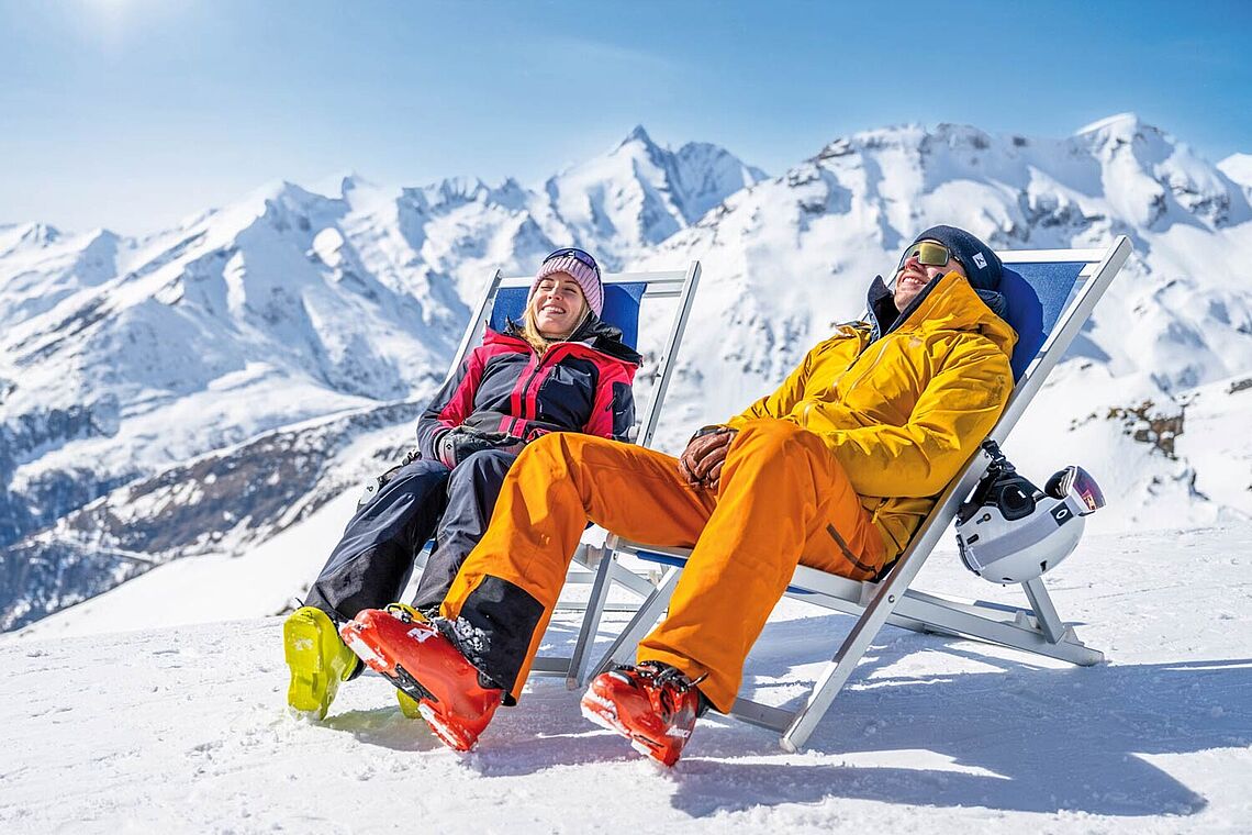 Zwei Skifahrer sitzen in Liegestühlen in der Sonne im Schnee