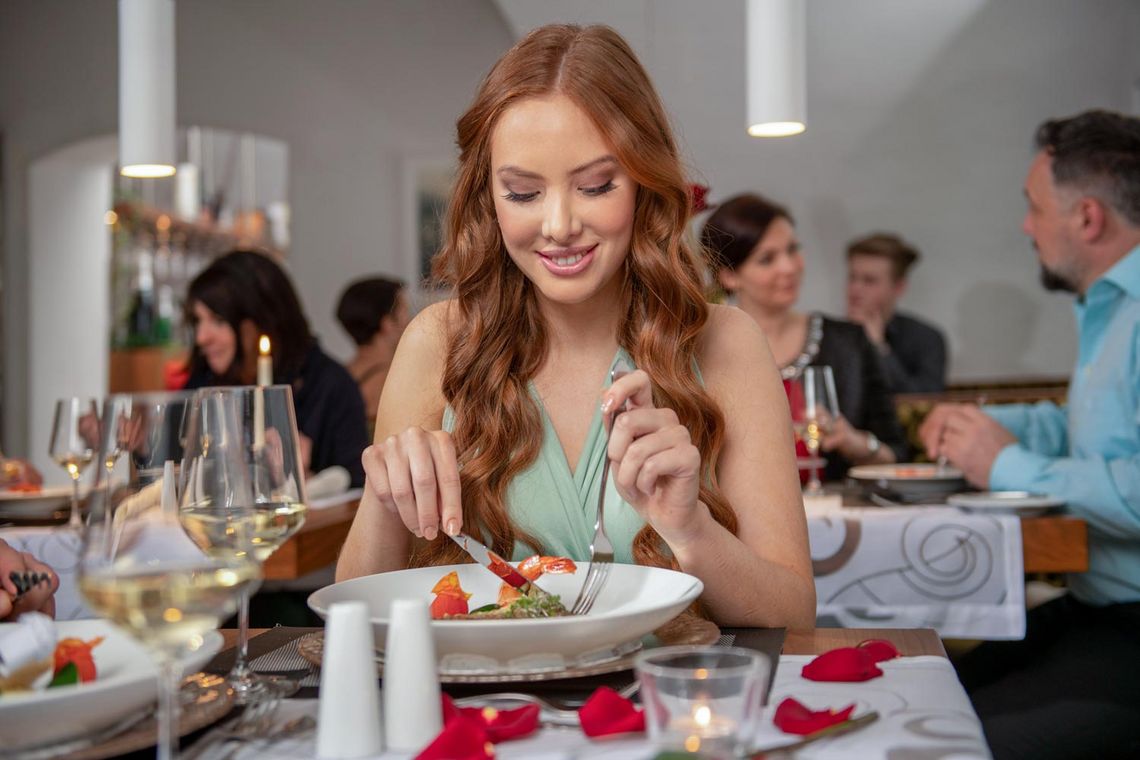 Junge Frau beim Abendessen mit Teller mit Garnelen und einem Glas Weißwein