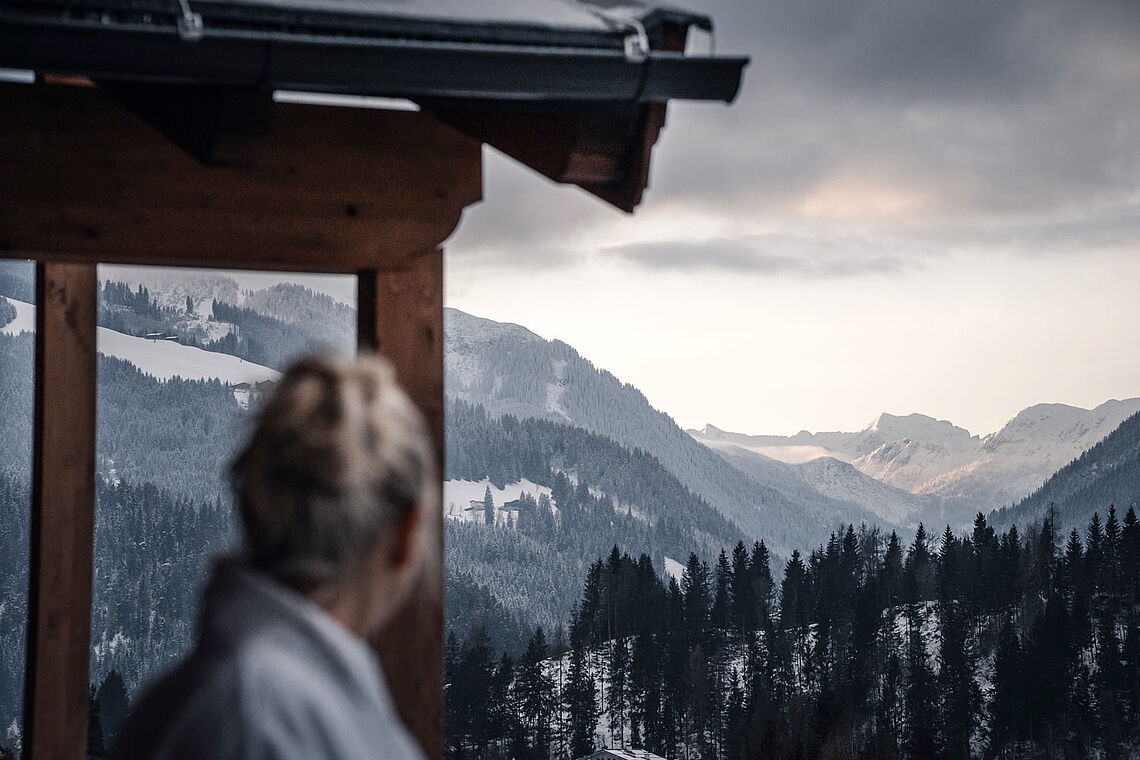 Frau schaut vom Balkon aus auf winterliche Berge