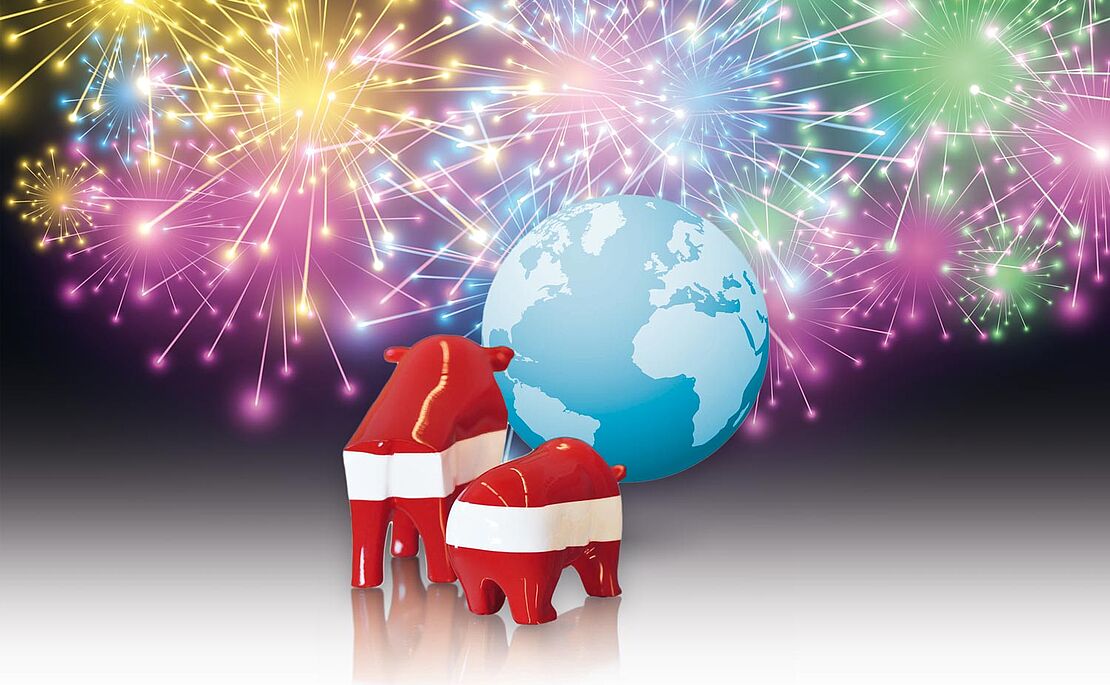 Bulle und Bär in rot-weiß-rot stehen vor einem Global, dahinter Feuerwerk