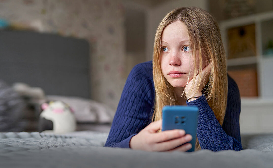 Junges Mädchen liegt mit ihrem Handy im Bett