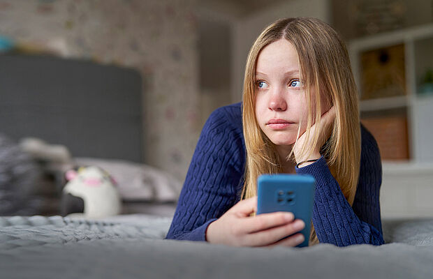 Junges Mädchen liegt mit ihrem Handy im Bett