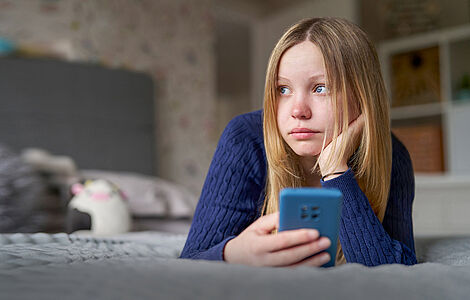 Junges Mädchen liegt mit ihrem Handy im Bett