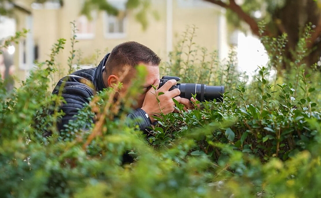 Ein im Gebüsch versteckter Mann beim Fotografieren