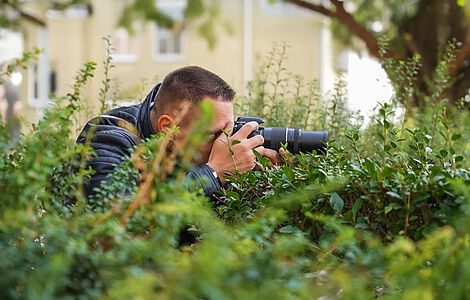 Ein im Gebüsch versteckter Mann beim Fotografieren