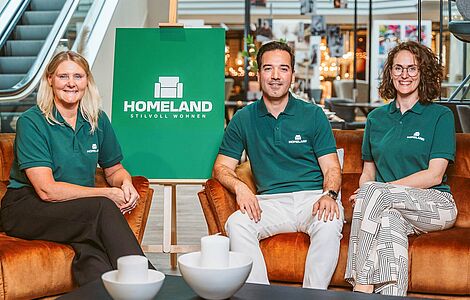 Fatima Gustafsson, Turgut Mermertas und Caroline Iselor sitzen alle in einem grünen Homeland Leiberl in einer Filiale