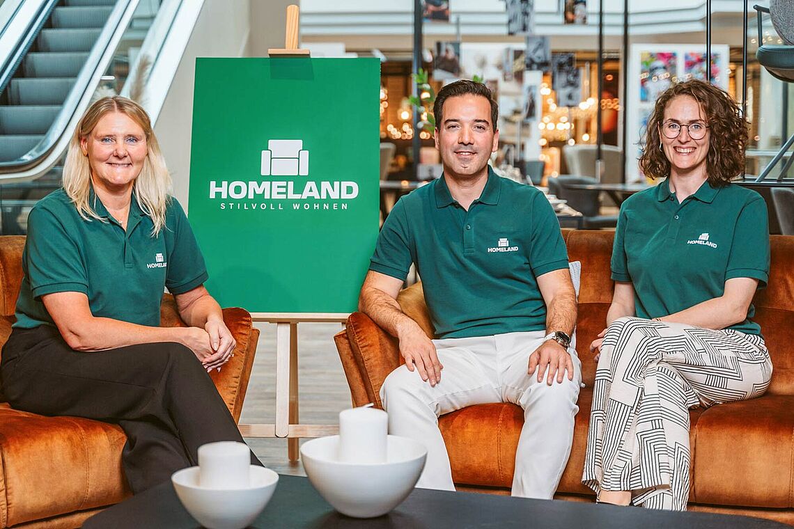 Fatima Gustafsson, Turgut Mermertas und Caroline Iselor sitzen alle in einem grünen Homeland Leiberl in einer Filiale