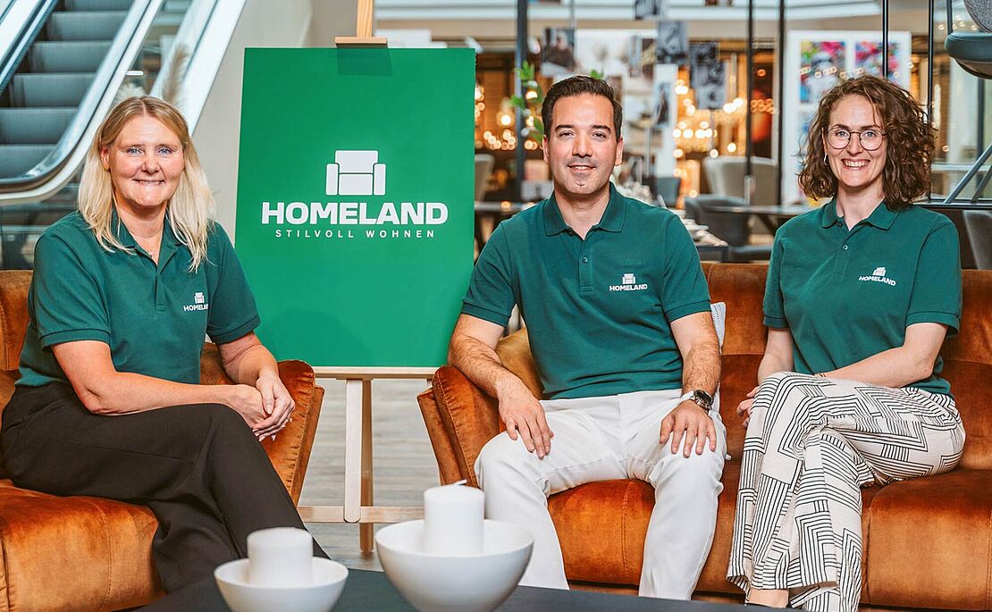 Fatima Gustafsson, Turgut Mermertas und Caroline Iselor sitzen alle in einem grünen Homeland Leiberl in einer Filiale