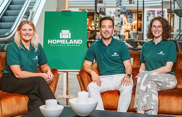Fatima Gustafsson, Turgut Mermertas und Caroline Iselor sitzen alle in einem grünen Homeland Leiberl in einer Filiale