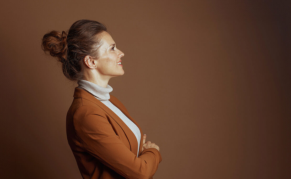 Frau mit Dutt hellem Rollkragenpulli und braunem Blazer seitwärts gerichtet, blickt nach oben