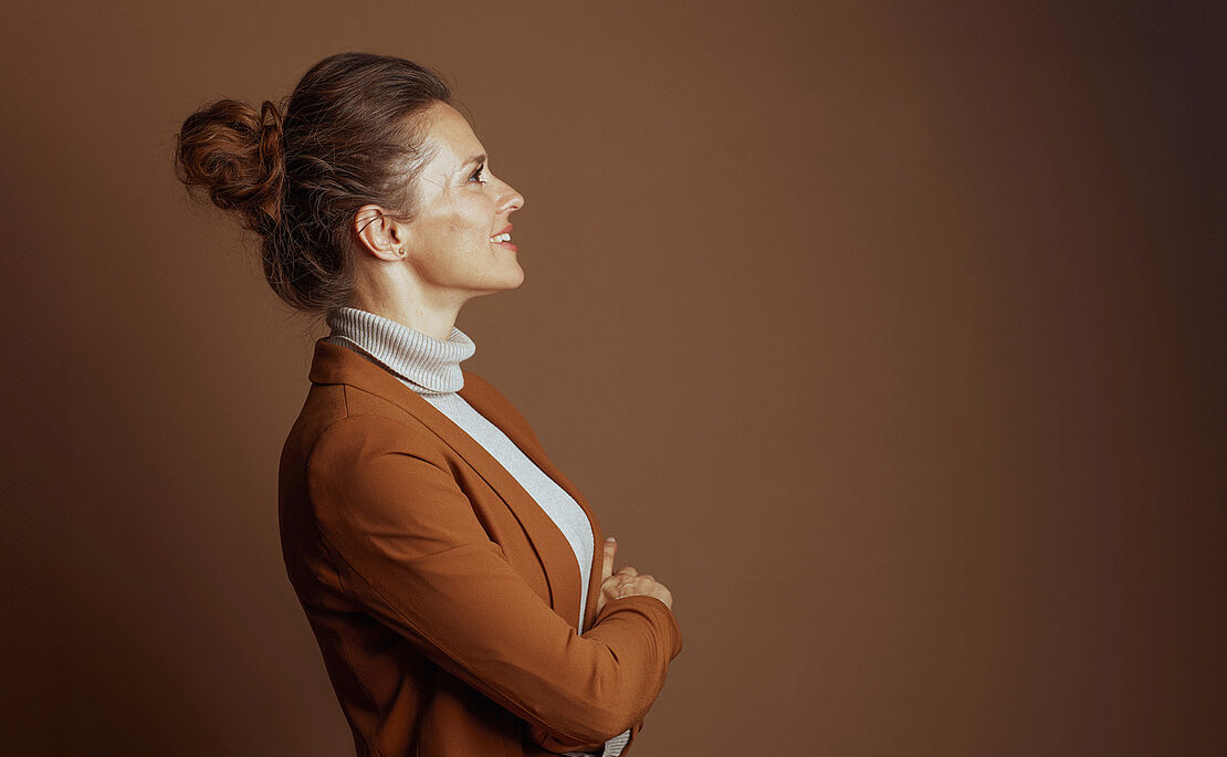 Frau mit Dutt hellem Rollkragenpulli und braunem Blazer seitwärts gerichtet, blickt nach oben