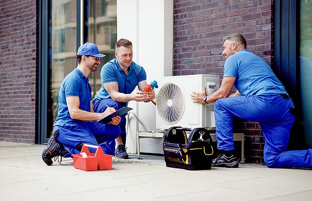 Drei Monteure in blauer Kleidung, die eine Wärmepumpe installieren