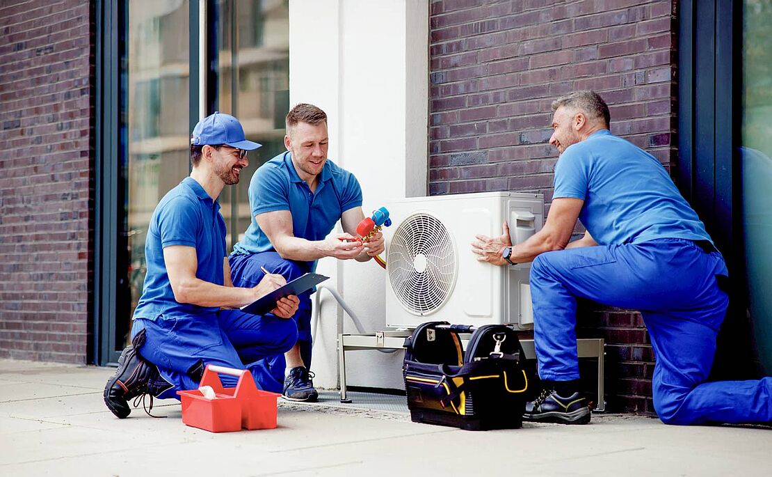 Drei Monteure in blauer Kleidung, die eine Wärmepumpe installieren