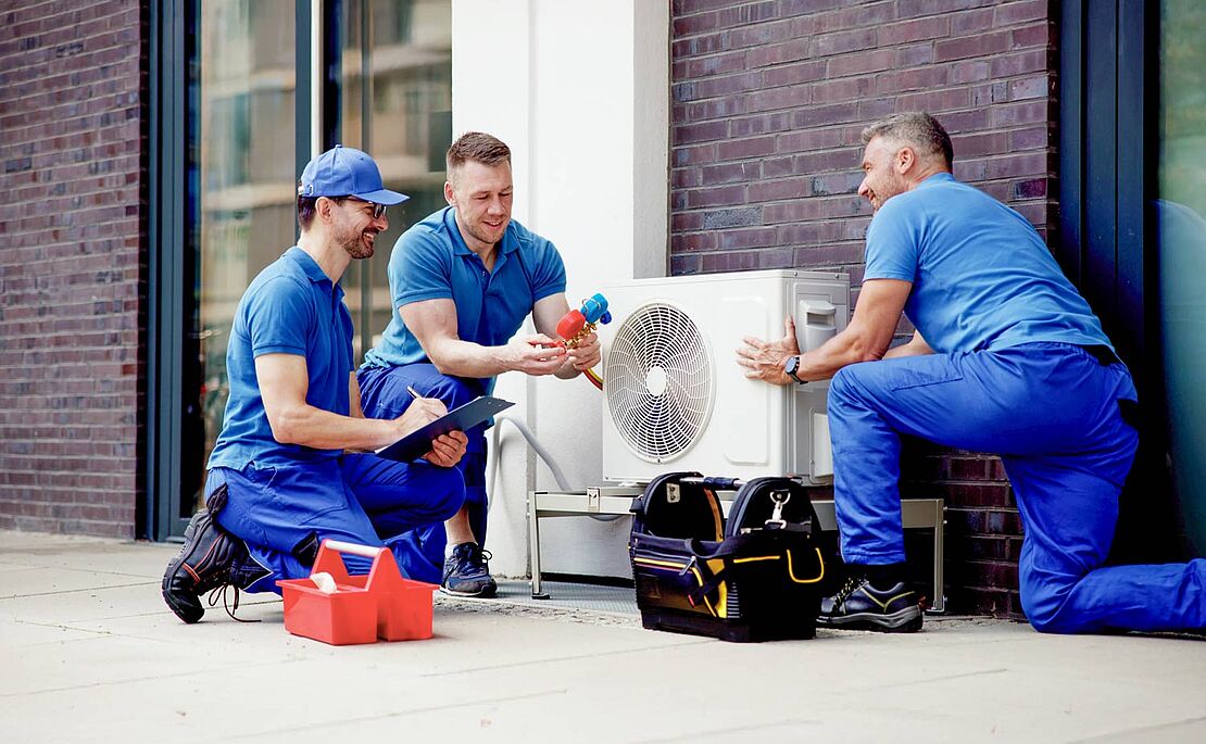 Drei Monteure in blauer Kleidung, die eine Wärmepumpe installieren