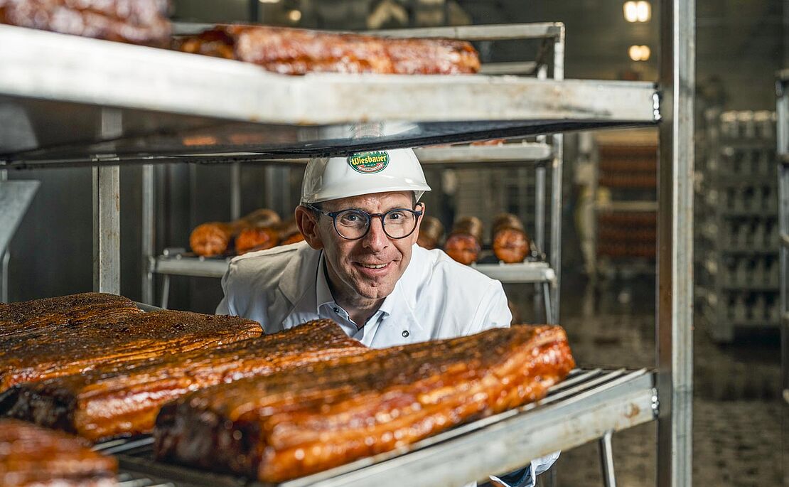 Thomas Schmidbauer schaut durch Regale mit Speck durch