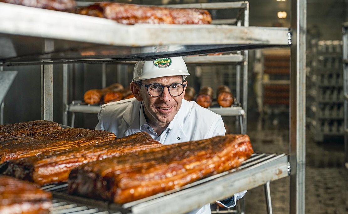 Thomas Schmidbauer schaut durch Regale mit Speck durch