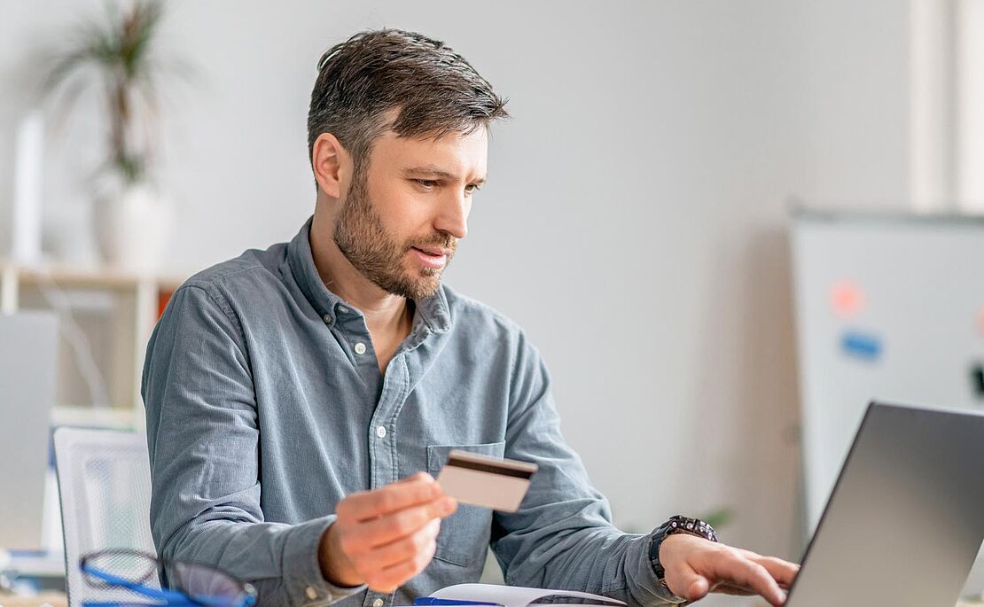 Mann mit Plastikkarte in der Hand vor Laptop