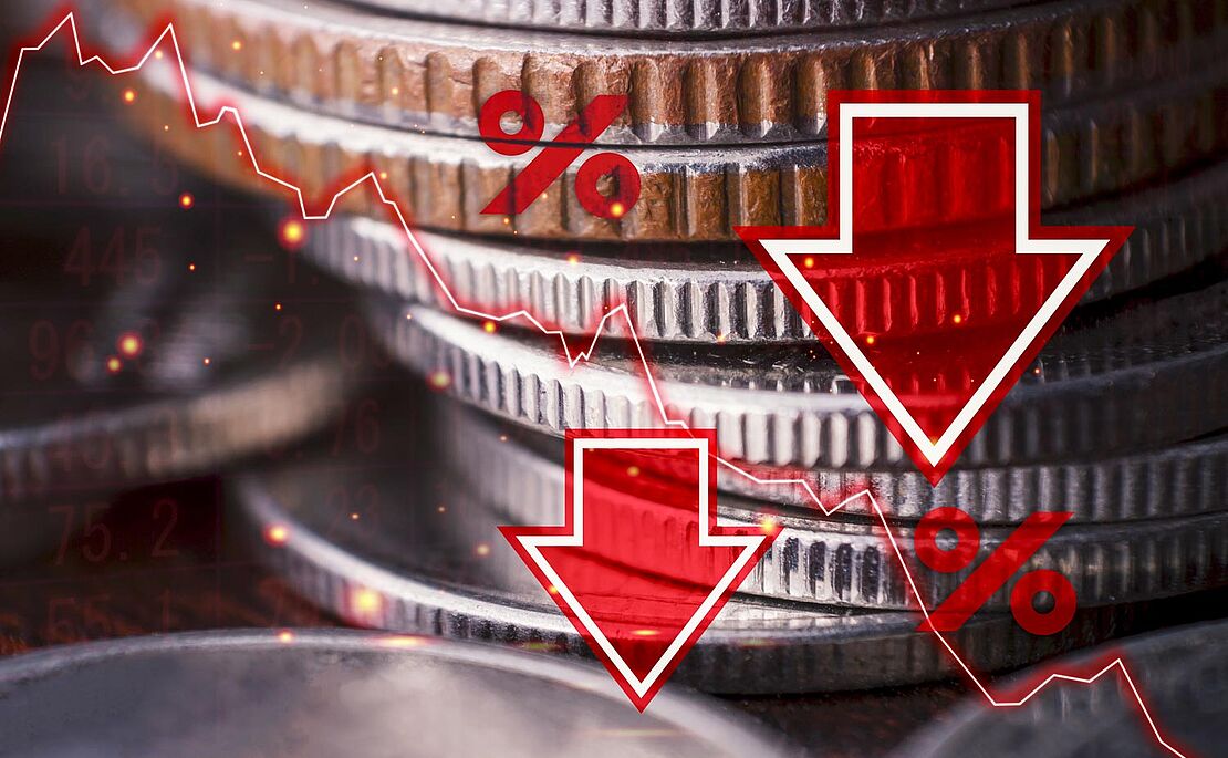 Herangezoomtes Foto eines Münzstapels, darüber sind mit Bildbearbeitung zwei rote nach unten zeigende Pfeile, zwei Prozentzeichen und eine fallende Kurskurve gelegt