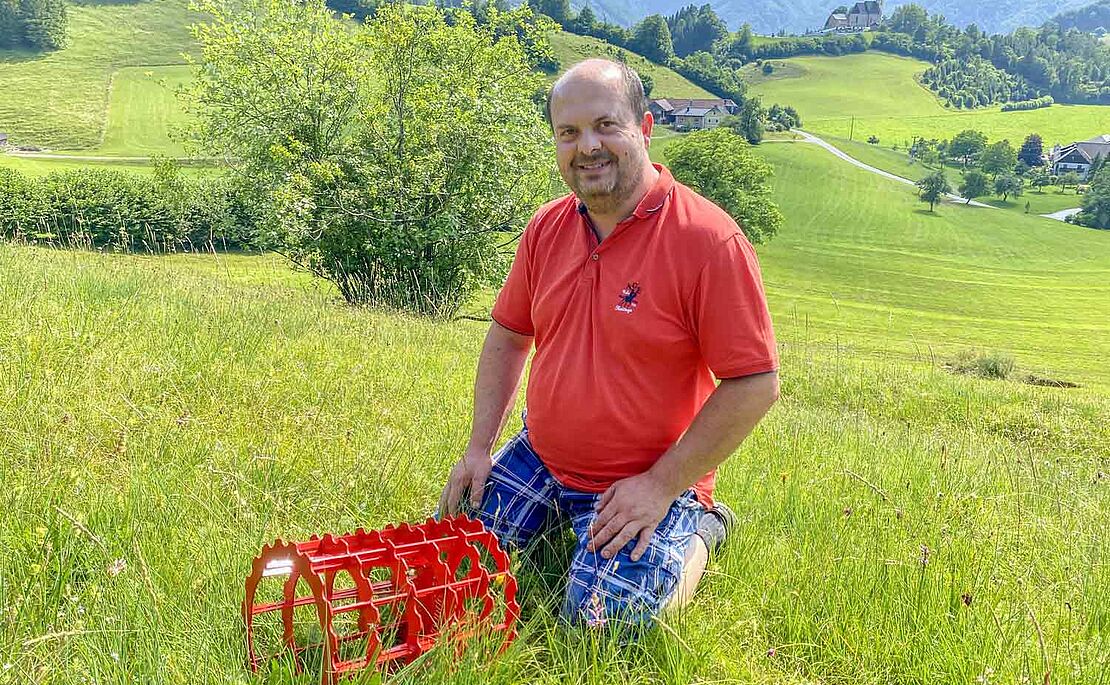 Stefan Edtbauer auf einer Wiese knieend, davor sein Roundgrip-Metallreifen in rot