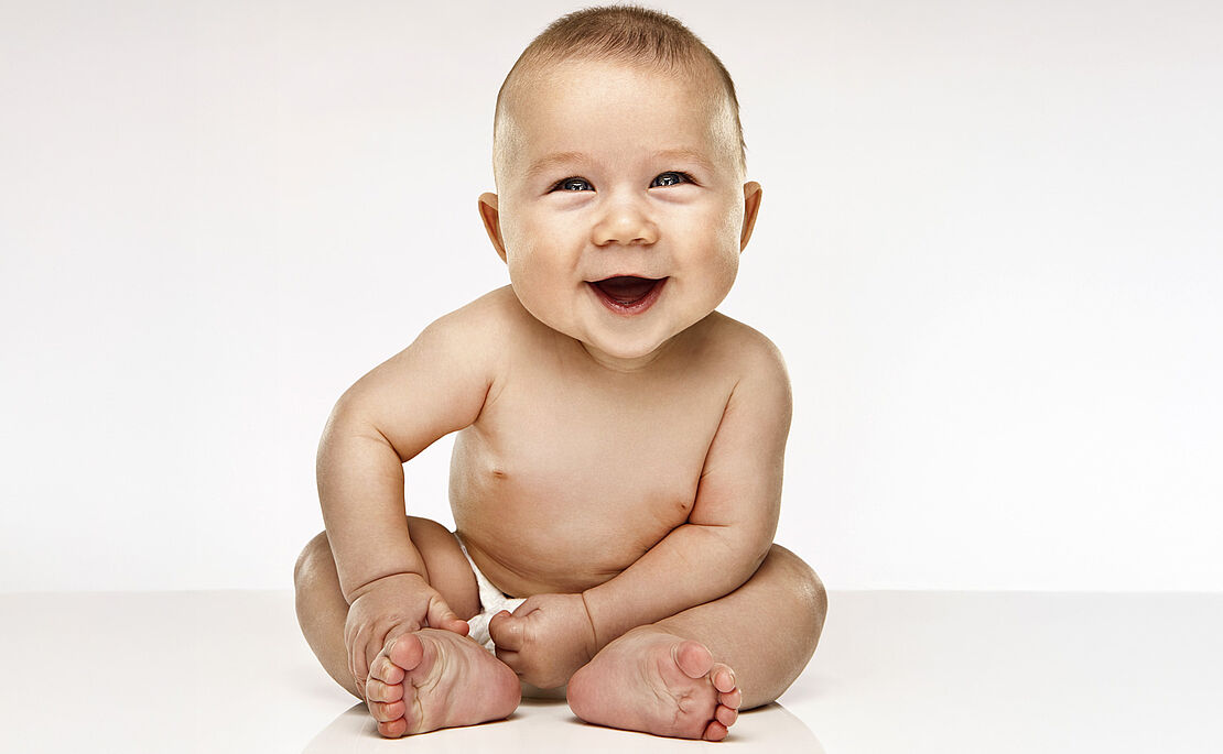 Ein nacktes Baby sitzt und lacht