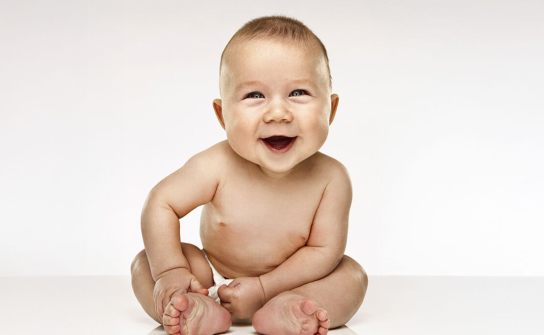 Ein nacktes Baby sitzt und lacht