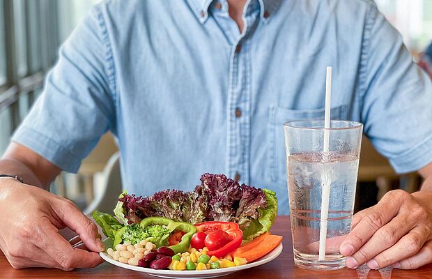 Mann sitzt vor einem Teller mit gesundem Gemüse und einem Glas Wasser