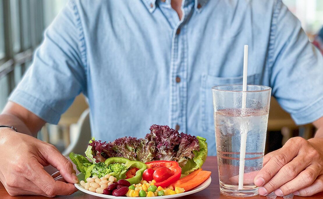 Mann sitzt vor einem Teller mit gesundem Gemüse und einem Glas Wasser