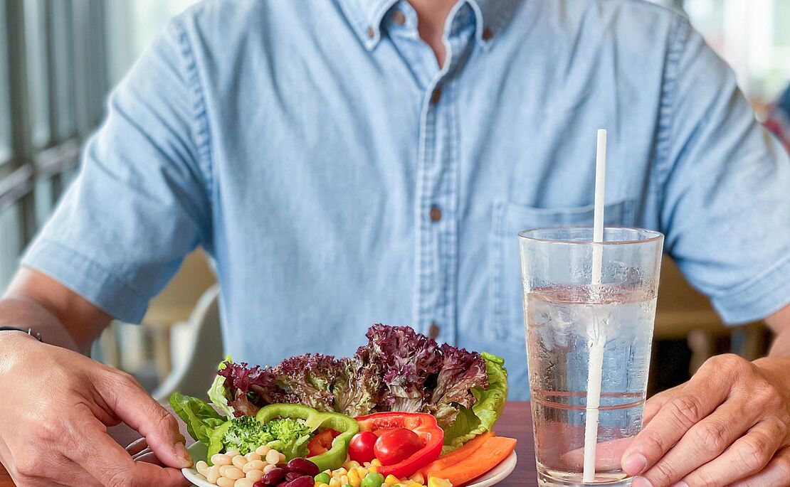 Mann sitzt vor einem Teller mit gesundem Gemüse und einem Glas Wasser