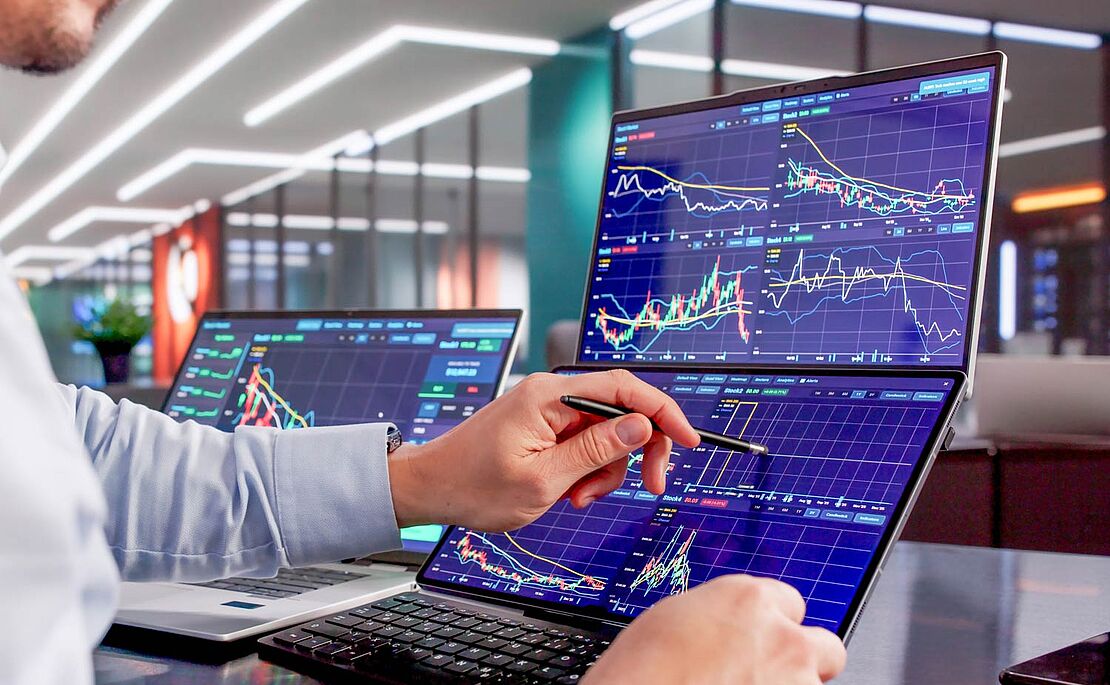 Hände mit einem Stift in der Hand, die auf einem Display mit vielen Grafiken tippen