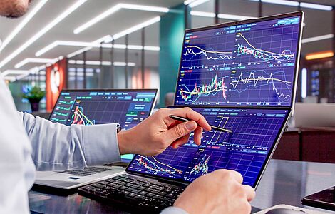 Hände mit einem Stift in der Hand, die auf einem Display mit vielen Grafiken tippen