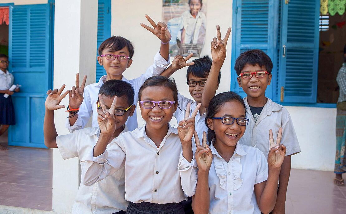 Gruppe von sechs Schulkindern, alle mit Brille, alle machen das Victoryzeichen
