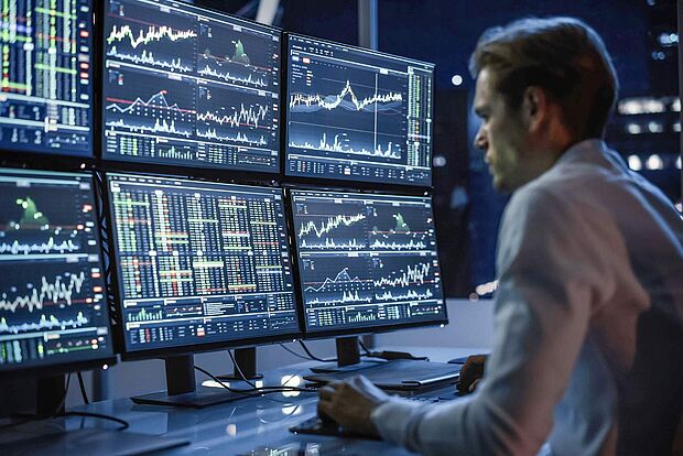 Mann vor 6 Bildschirmen mit diversen Charts
