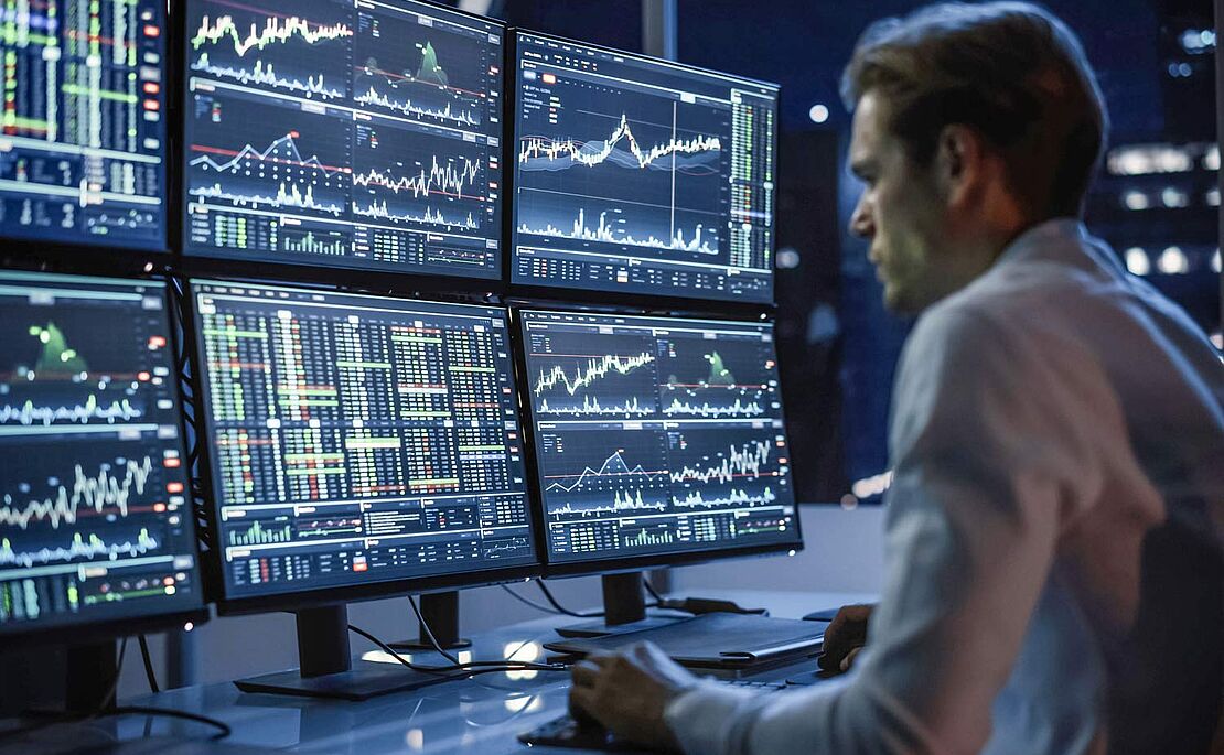Mann vor 6 Bildschirmen mit diversen Charts
